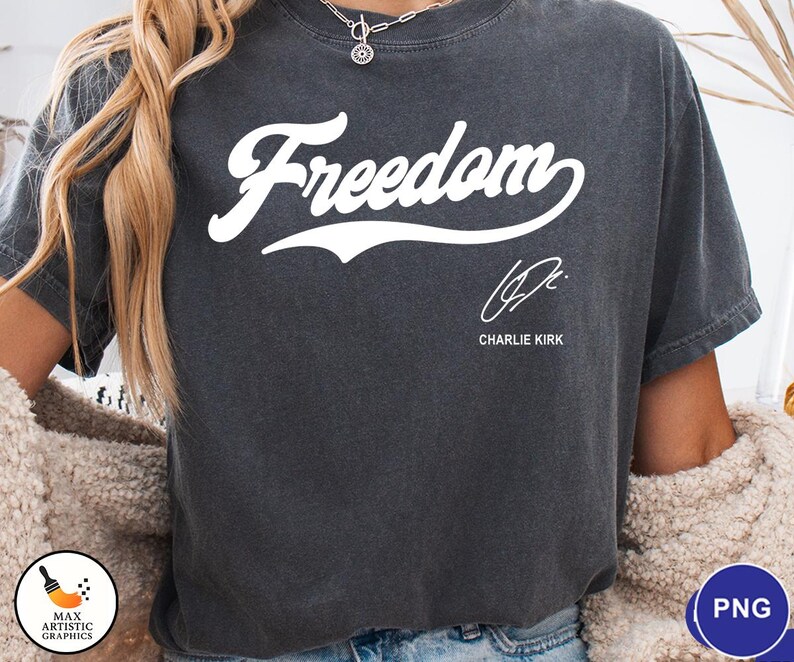 May include: Dark gray t-shirt with the word "Freedom" in white script. Below the word is a signature and the name "Charlie Kirk". The shirt is a casual style.