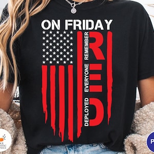 May include: Black t-shirt featuring a distressed American flag design in red and white. The text "ON FRIDAY REMEMBER EVERYONE DEPLOYED RED" is printed on the shirt. The shirt has a crew neck and short sleeves.