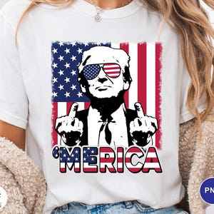 May include: White t-shirt featuring a graphic of a man wearing sunglasses with the American flag design. The man is giving the middle finger with both hands. The word "'MERICA" is printed in red, white, and blue.