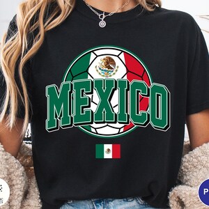 May include: A black t-shirt featuring a large graphic of a soccer ball colored with the green, white, and red of the Mexican flag. The word MEXICO is printed in large green block letters with white outlines. A small Mexican flag is centered below.