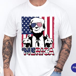 May include: White t-shirt featuring a graphic of a man wearing sunglasses with an American flag design. The man is giving the middle finger with both hands. The word "'MERICA" is printed in red, white, and blue.