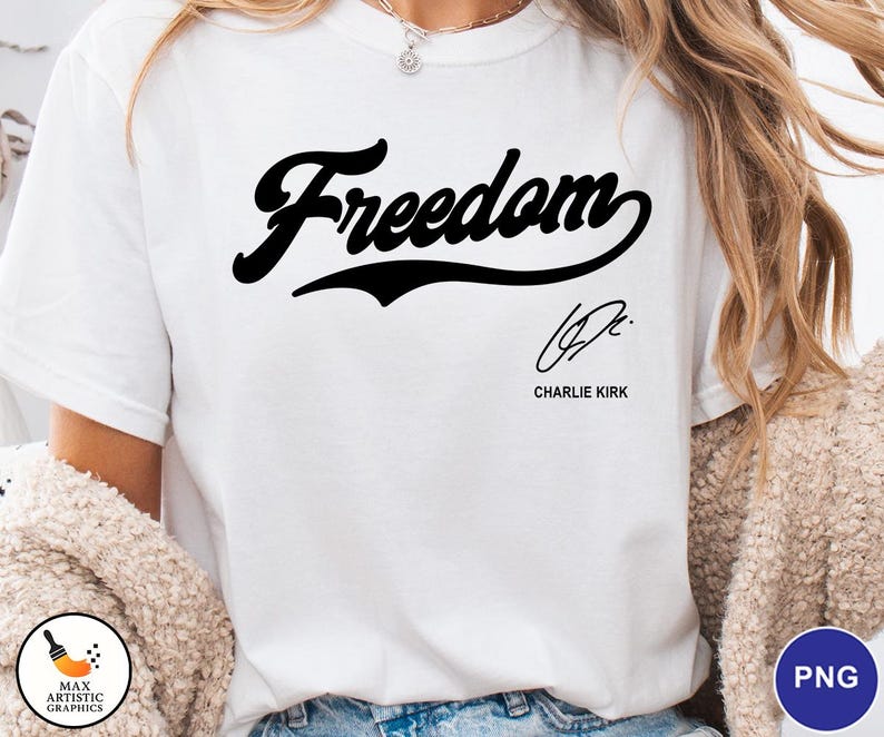 May include: White t-shirt with the word "Freedom" in a black script font. Below the word is a signature and the name "Charlie Kirk" in a smaller font. The shirt is a casual style.