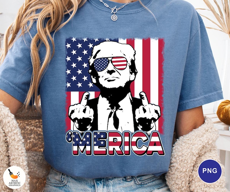 May include: Blue t-shirt featuring a graphic of a man wearing sunglasses with an American flag design. The image includes the text "'MERICA" in red, white, and blue. The man is giving the middle finger with both hands.