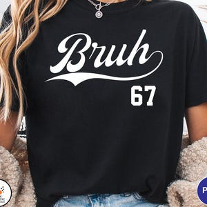 May include: Black t-shirt with the word "Bruh" in a white script font above the number "67". The shirt is a crew neck style and appears to be made of a soft material.