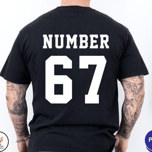 Op de afbeelding: Zwart T-shirt met het woord "NUMBER" boven het nummer "67" in witte blokletters. Het shirt heeft een klassieke ronde hals.