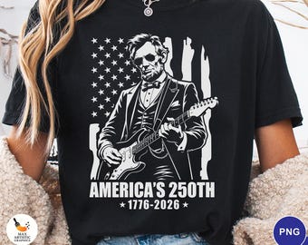 May include: Black t-shirt featuring a white graphic of Abraham Lincoln playing an electric guitar in front of an American flag. The text reads "AMERICA'S 250TH * 1776-2026 *."