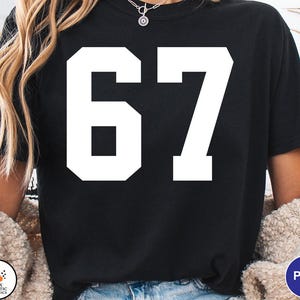 Op de afbeelding: Zwart T-shirt met het witte nummer 67 op de voorkant. Het nummer is in een vetgedrukte, blokletter. Het shirt is een casual stijl, geschikt voor dagelijks gebruik.