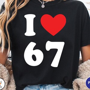 Op de afbeelding: Zwart T-shirt met de tekst "I ❤️ 67". De "I" en "67" zijn wit en het hart is rood. Het shirt heeft een casual stijl.