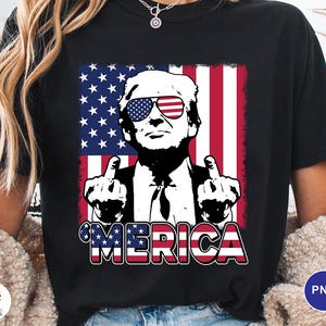 May include: Black t-shirt featuring a graphic of a man wearing sunglasses with the American flag design. The man is giving the middle finger with both hands. The word "'MERICA" is printed in red, white, and blue.