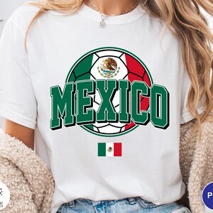 May include: A white short-sleeve t-shirt featuring a graphic of a soccer ball colored with the green, white, and red of the Mexican flag. The word MEXICO is printed in large green block letters across the center, with a small Mexican flag below.