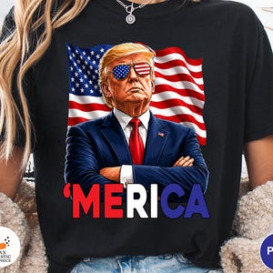 May include: Black t-shirt featuring a portrait of a man with sunglasses designed as the American flag, set against a waving American flag. The word "'MERICA" is printed in red, white, and blue.