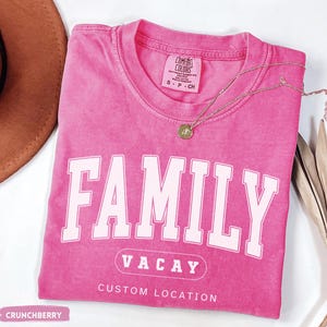 Peut inclure: Un t-shirt rose &agrave; manches courtes avec un col rond. Le t-shirt pr&eacute;sente le mot FAMILY en grandes lettres blanches, le texte VACAY dans un ovale et les mots CUSTOM LOCATION imprim&eacute;s en dessous en blanc. L'&eacute;tiquette indique COMFORT COLORS.