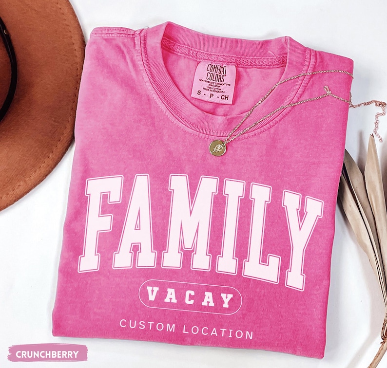 Peut inclure: Un t-shirt rose &agrave; manches courtes avec un col rond. Le t-shirt pr&eacute;sente le mot FAMILY en grandes lettres blanches, le texte VACAY dans un ovale et les mots CUSTOM LOCATION imprim&eacute;s en dessous en blanc. L'&eacute;tiquette indique COMFORT COLORS.