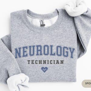 May include: A gray sweatshirt with the text "NEUROLOGY TECHNICIAN" in blue and black lettering. A small blue heart with a heartbeat symbol is below the text. The sweatshirt is labeled "SPORT GREY".