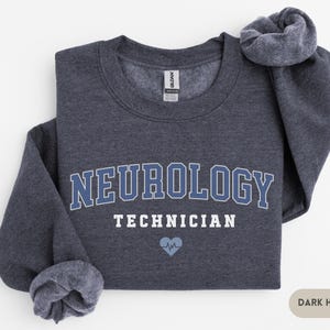 May include: Dark heather grey sweatshirt with the text "Neurology Technician" in white and a blue heart with a heartbeat symbol.