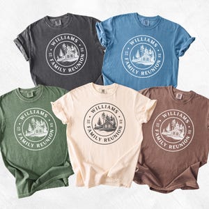May include: Five short-sleeve crew neck t-shirts in charcoal, blue, green, cream, and brown. Each shirt features a circular graphic with a cabin, pine trees, and the text "WILLIAMS FAMILY REUNION" along with "EST" and "2026" on the sides.