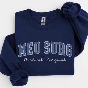 May include: Navy blue sweatshirt with the text "MED SURG" in a collegiate font, with "Medical - Surgical" below. The sweatshirt is a crew neck style.