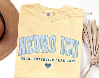 May include: A butter yellow short-sleeve t-shirt featuring the text NEURO ICU in large, light blue, vertically striped collegiate-style letters, with the words NEURO INTENSIVE CARE UNIT and a small blue heart with an EKG line below.