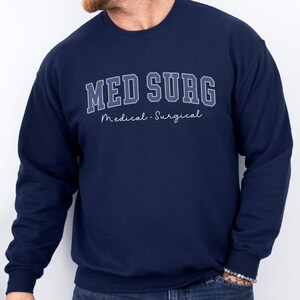 May include: Navy blue sweatshirt with the text "MED SURG" in a collegiate style font, with the words "Medical - Surgical" underneath. The sweatshirt is a solid navy blue color.