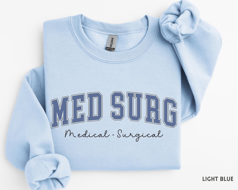 May include: Light blue sweatshirt with the text "MED SURG" in a navy blue collegiate font, with "Medical - Surgical" written below in a script font. The sweatshirt is folded, with the sleeves rolled up.