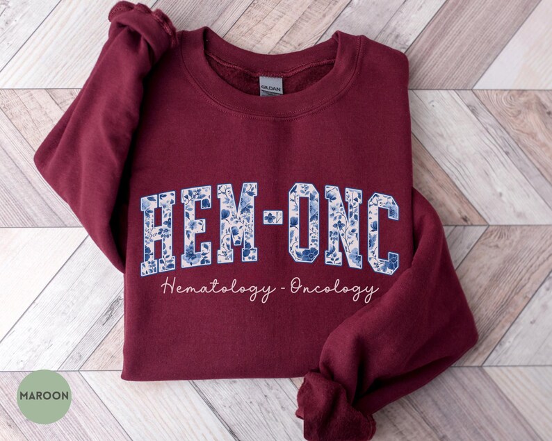 May include: Maroon sweatshirt with the text "HEM-ONC" in white letters filled with a blue floral pattern. Below the text is the script "Hematology - Oncology". The word "MAROON" is in a green circle in the lower left corner.