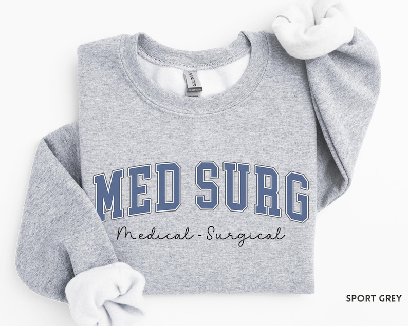 May include: Sport grey sweatshirt with the text "MED SURG" in blue block letters with a white outline. Below the text is "Medical - Surgical" in a cursive font. The sweatshirt has white fleece lining the collar and cuffs.
