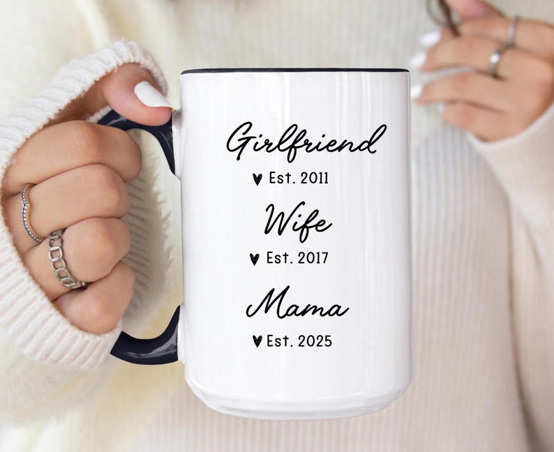 May include: White ceramic mug with black text that reads "Girlfriend Est. 2011, Wife Est. 2017, Mama Est. 2025".