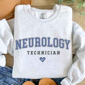 May include: A gray sweatshirt with the text "NEUROLOGY TECHNICIAN" in blue and black lettering. A small blue heart with a heartbeat symbol is below the text.