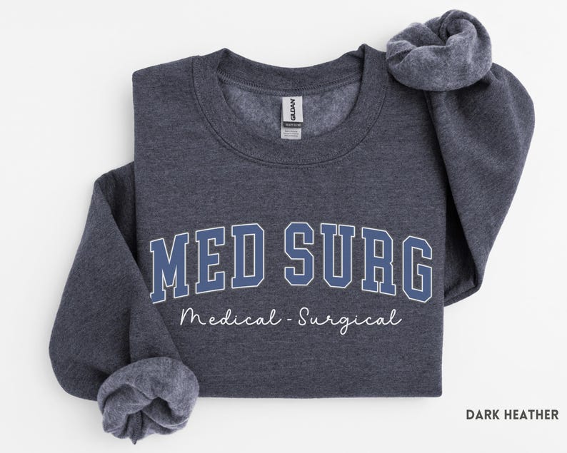 May include: Dark heather gray sweatshirt with the text "MED SURG" in blue block letters with a white outline. Below the text is the phrase "Medical - Surgical" in a cursive font. The sweatshirt is folded.