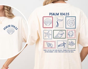May include: Cream-colored t-shirt featuring a seashell graphic and the text "PSALM 104:25" on the front. The back displays a series of marine life illustrations within postage stamp-like frames, with accompanying text about the sea.