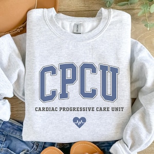 May include: A gray sweatshirt with the text "CPCU Cardiac Progressive Care Unit" and a blue heart with a heartbeat symbol.