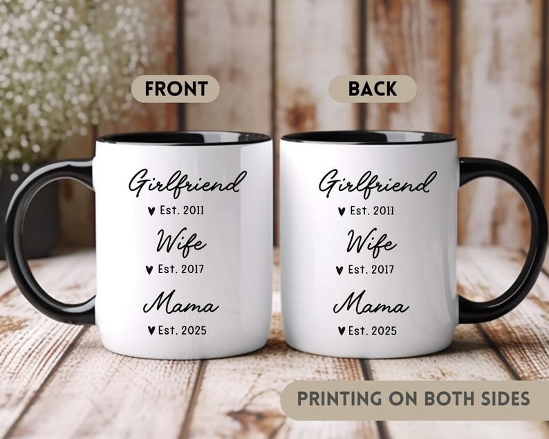 May include: White ceramic mug with a black handle and black rim. The mug has black text that reads "Girlfriend Est. 2011 Wife Est. 2017 Mama Est. 2025". The mug is printed on both sides.