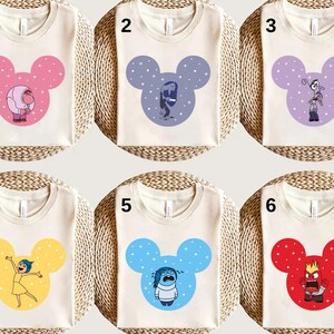 May include: Six off-white t-shirts with different coloured Mickey Mouse head designs featuring characters from the film "Inside Out." Each design has a different character in the centre of the Mickey Mouse head.