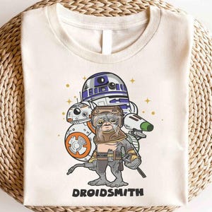 Op de afbeelding: Een wit T-shirt met een cartoon afbeelding van Star Wars-personages R2-D2, BB-8 en een droid met de tekst "DROIDSMITH" gedrukt aan de onderkant.