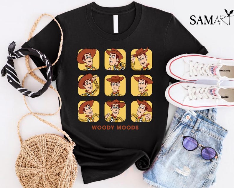 以下が含まれることがあります： トイストーリーのウッディの顔が9つ並んだ、黒いTシャツ。それぞれのウッディは異なる表情をしています。グリッドの下には「WOODY MOODS」という文字が印刷されています。