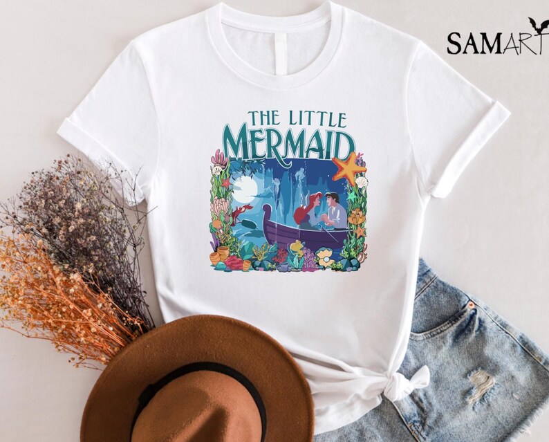 Puede incluir: Camiseta blanca con un gr&aacute;fico colorido de "La Sirenita". El dise&ntilde;o incluye el t&iacute;tulo, un barco con personajes y elementos submarinos. La camiseta est&aacute; hecha de un material suave y tiene mangas cortas.