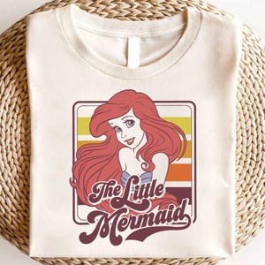 May include: A white t-shirt with a retro-style graphic of Ariel, the Little Mermaid, with the text "The Little Mermaid" in a vintage font.