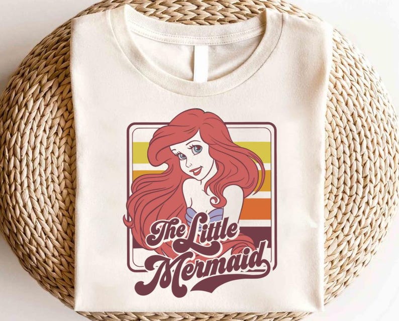 May include: A white t-shirt with a retro-style graphic of Ariel, the Little Mermaid, with the text "The Little Mermaid" in a vintage font.