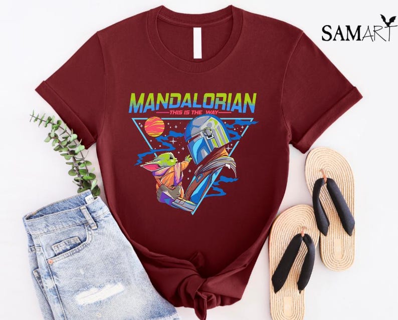 May include: A maroon t-shirt with a graphic of a Mandalorian and Grogu. The graphic is in a retro style with a triangle and the text "Mandalorian - This is the Way".
