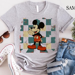 May include: A gray t-shirt with a vintage-style image of Mickey Mouse on a checkered background. The image is in shades of red, blue, green, and yellow.