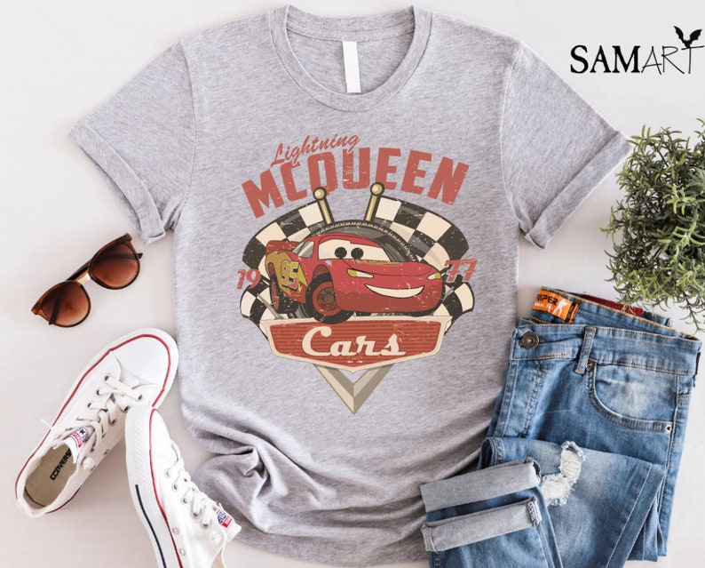 Op de afbeelding: Grijs T-shirt met een rode racewagen afbeelding en de tekst "Lightning McQueen Cars".