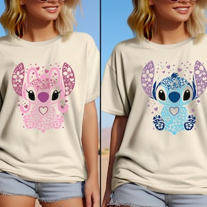 May include: Two white t-shirts with a cartoon Stitch design. One shirt features a pink Stitch with floral details and the other features a blue Stitch with floral details.