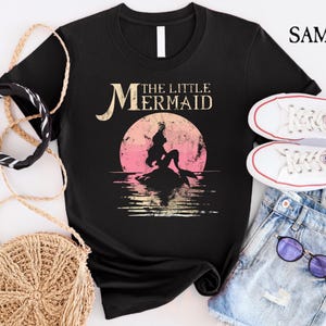 May include: Black t-shirt with a vintage-style graphic of a mermaid with the text "The Little Mermaid" in white.