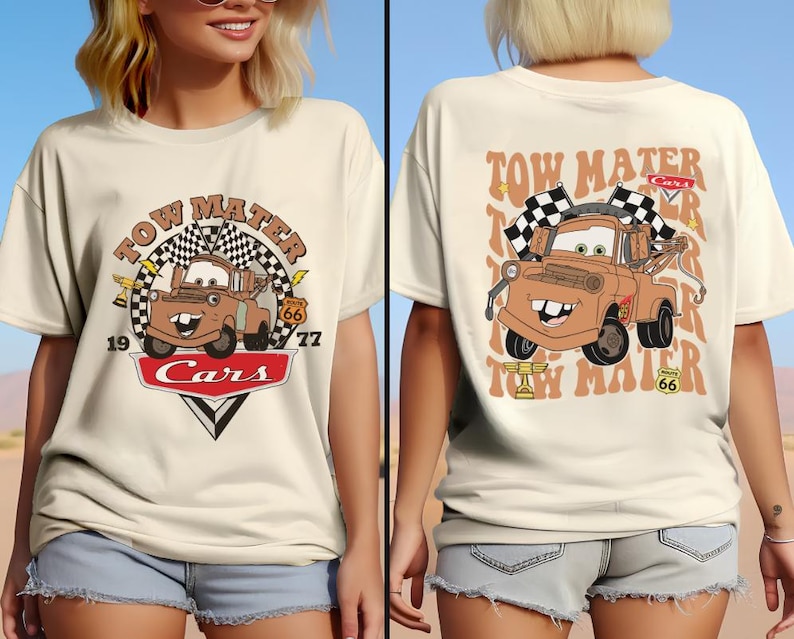May include: A beige t-shirt with a graphic of Tow Mater from the Cars movie. The graphic features Tow Mater with the text "Tow Mater" and "Cars" in a red circle with a checkered flag design. The text "Tow Mater" is also printed on the back of the shirt.