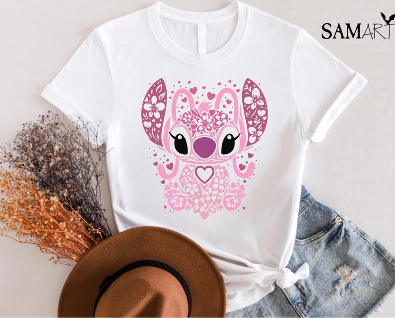 May include: White t-shirt with a pink and white floral design of a cartoon character with big eyes and a heart. The character is surrounded by hearts.