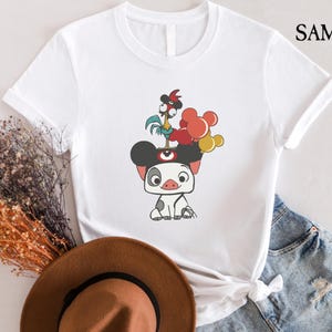 May include: White t-shirt featuring a cartoon illustration of a pig with a rooster on its head and red, yellow, and orange balloons. The shirt has the word "SAMART" printed on the upper right side.