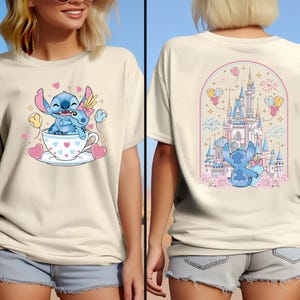 May include: Cream-colored t-shirt featuring a cartoon Stitch design. The front shows Stitch and a companion in a teacup with hearts. The back displays Stitch in front of a castle with fireworks and balloons.
