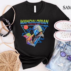 May include: Black t-shirt with a retro-style graphic of the Mandalorian and Grogu. The graphic features the text "Mandalorian - This is the Way" in a colorful font.