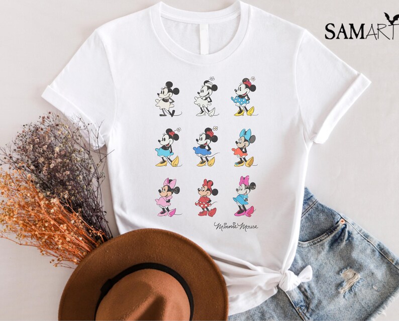 May include: White t-shirt with a graphic of nine different Minnie Mouse characters in various poses. The text "Minnie Mouse" is printed at the bottom of the shirt.