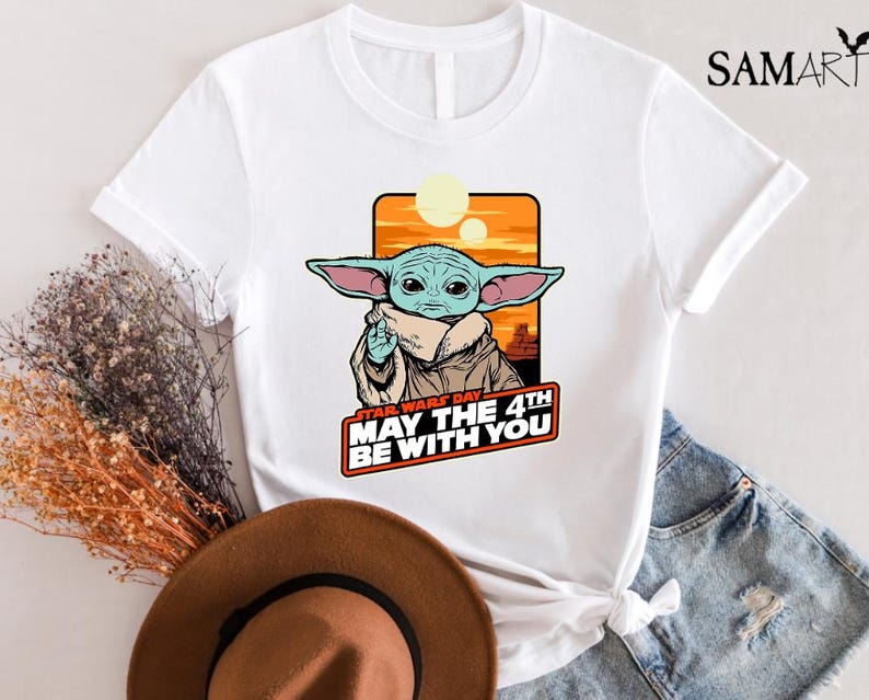 May include: White t-shirt with a cartoon image of a green alien character from Star Wars. The text "Star Wars Day May the 4th Be With You" is printed on the shirt.